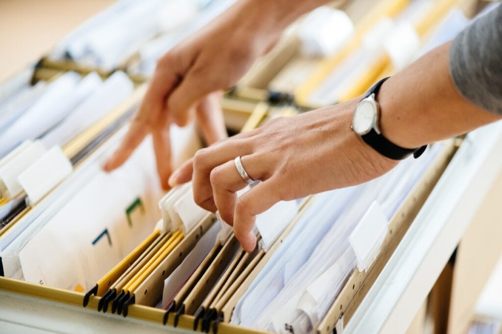 A person's hands sorting through a file cabinet filled with documents and folders, meticulously conducting comprehensive background checks.