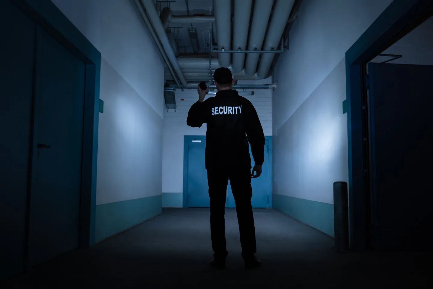 A security guard stands in a dimly lit hallway, holding a flashlight, with "SECURITY" visible on the back of the uniform.