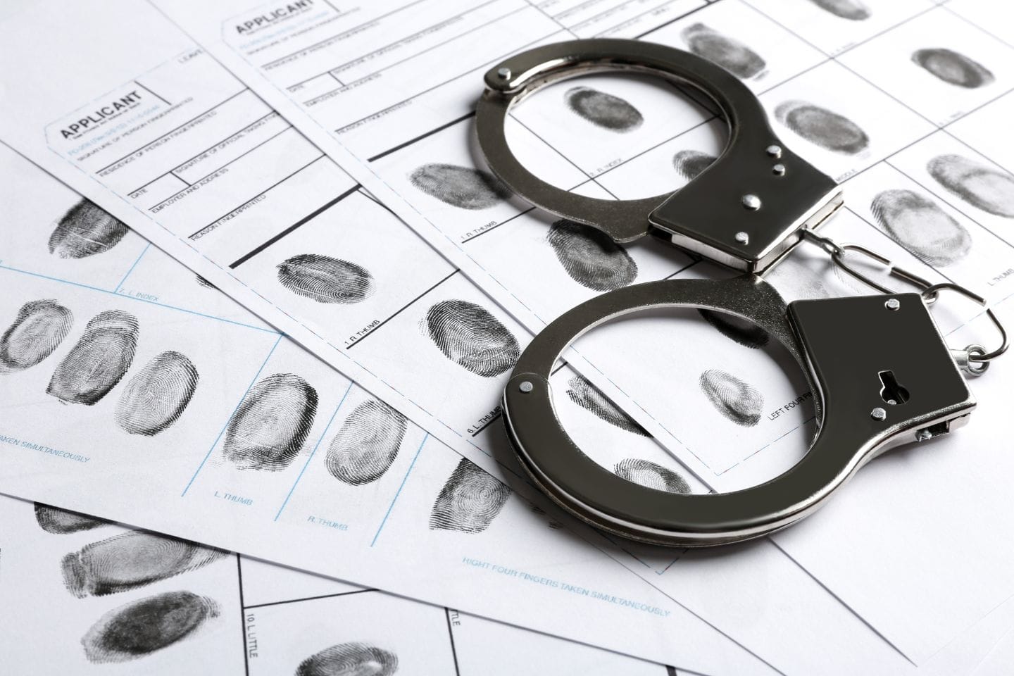 Handcuffs lie on fingerprint sheets, displaying various fingerprints in black ink.