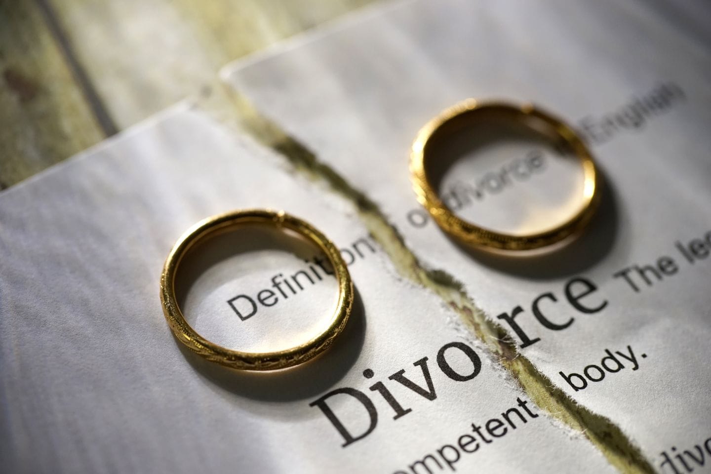 Two gold rings placed on a torn divorce document on a wooden surface.