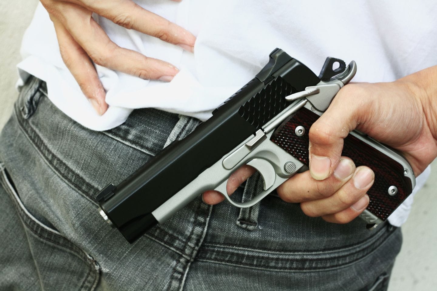 A person in jeans and a white shirt holds a handgun near their waist.