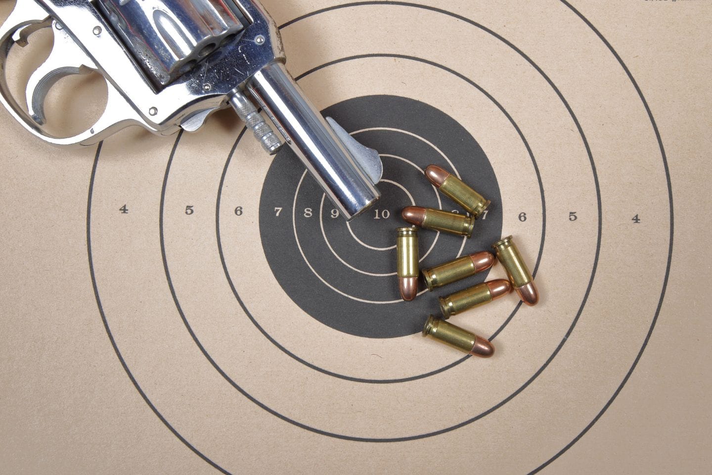 Revolver and scattered bullets on a paper target with concentric circles and numbers, indicating a shooting range setting.