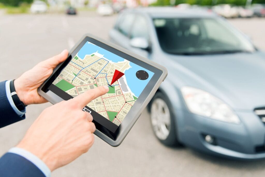 A person uses a tablet with a map application, pointing to a location. A parked blue car is in the background.