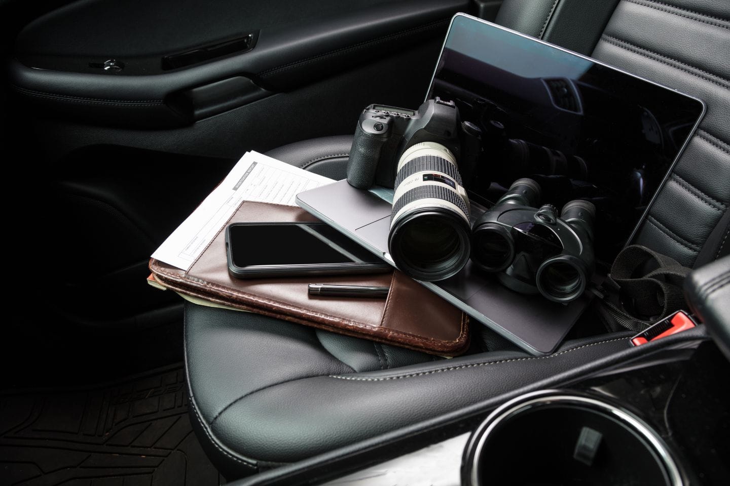 Car seat with a camera, binoculars, phone, pen, and documents on a laptop.