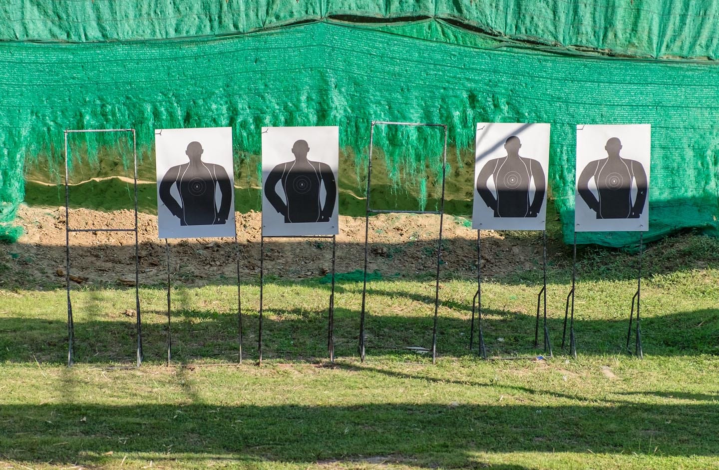 Five silhouette target sheets stand ready in front of a green barrier, poised for a dynamic shooter training session.