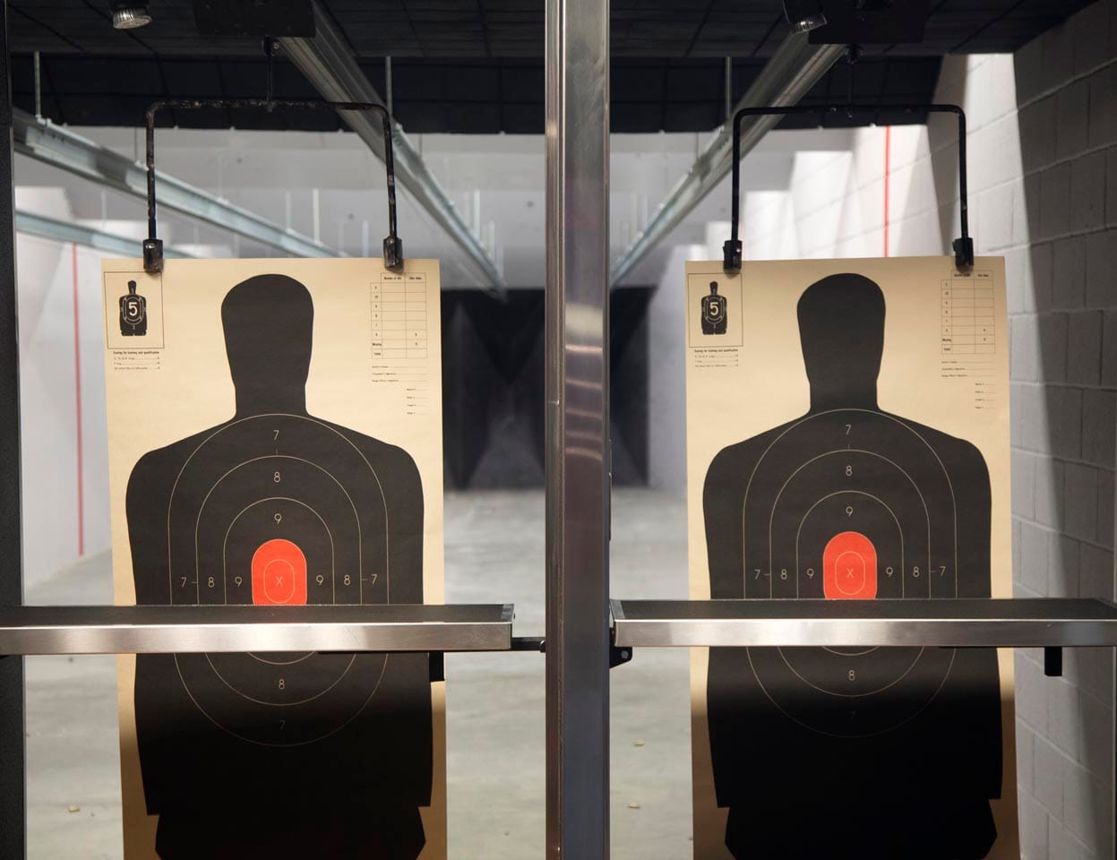 Two shooting range targets with human silhouettes are positioned side by side on a firing range, reflecting essential shooter response training.