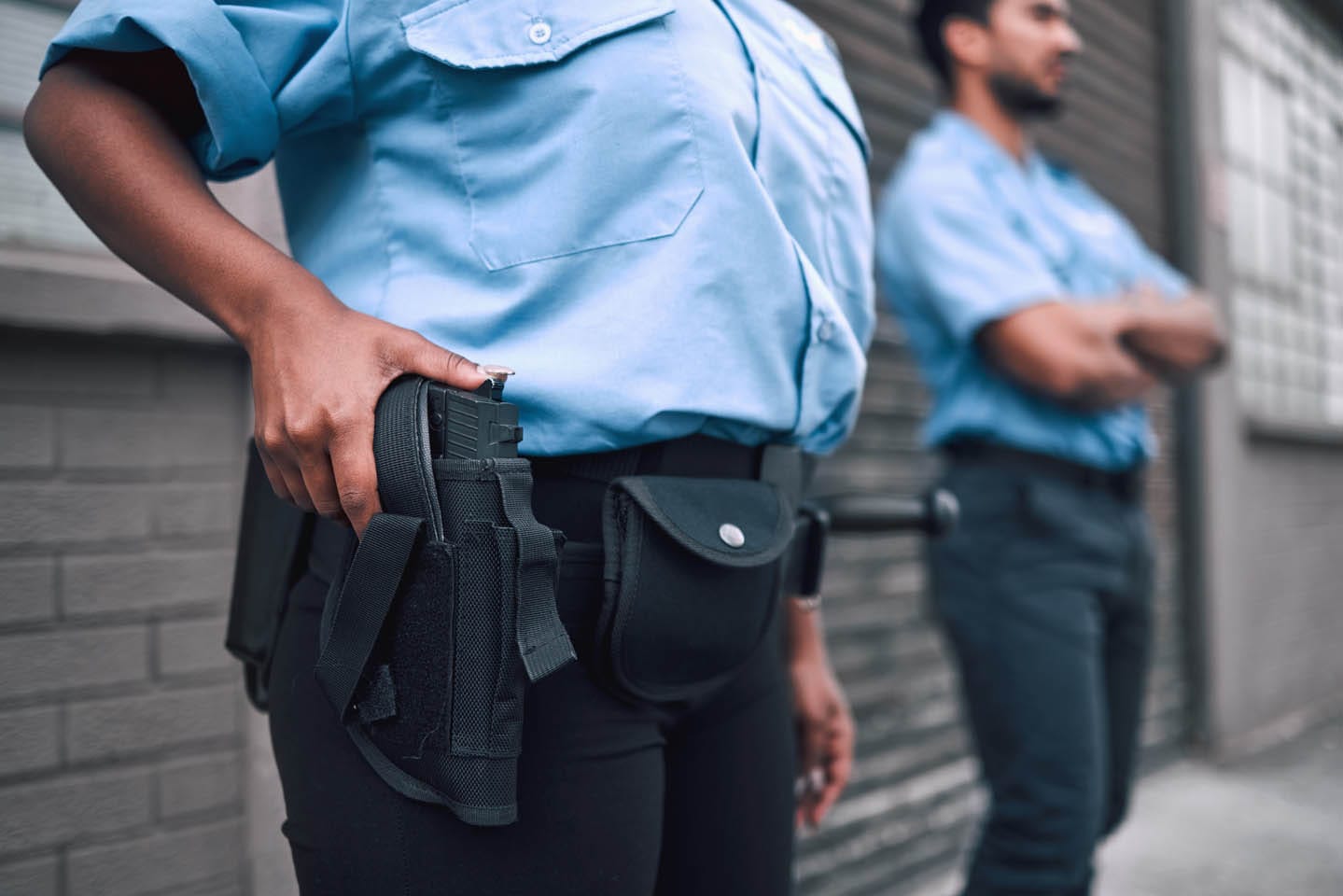 Two security guards in uniforms stand outside a building; one represents unarmed security while the other is holding a holstered handgun, showcasing armed security.