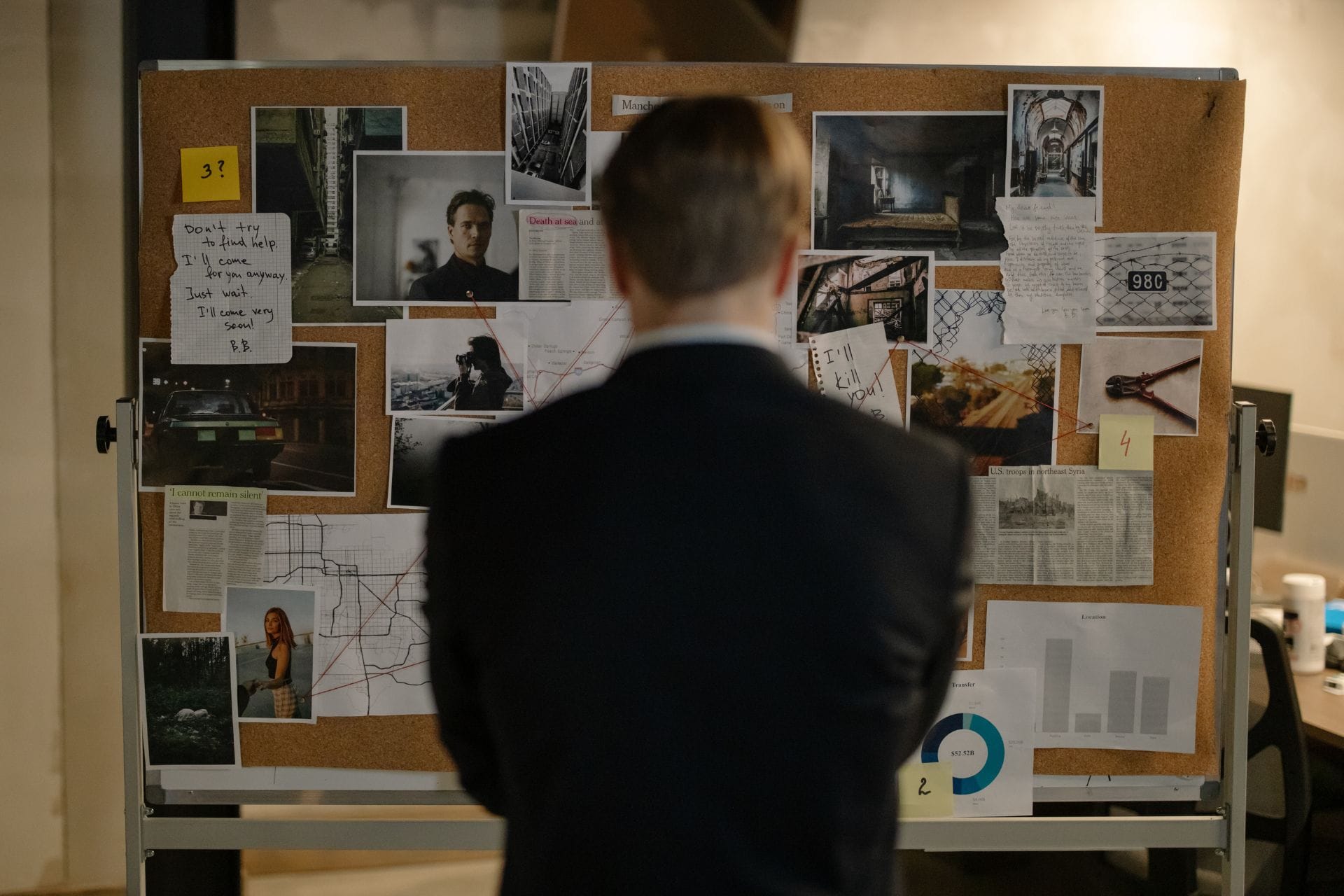 A person stands in front of a bulletin board filled with photos, notes, and documents.