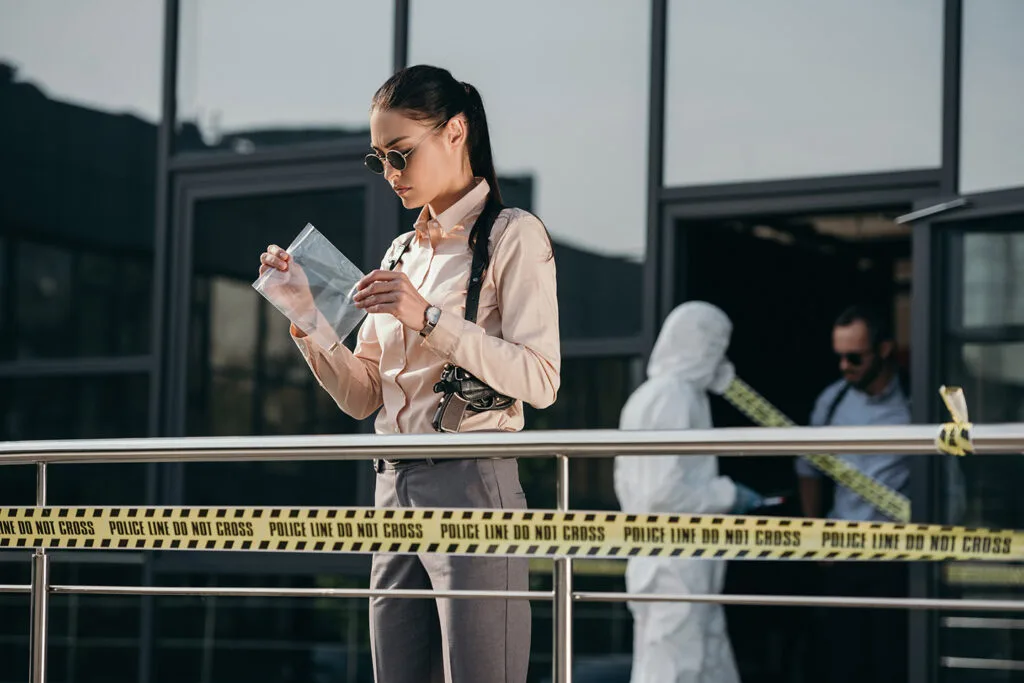 Investigator analyzing evidence at a corporate crime scene, with police tape in the foreground and forensic team in background, emphasizing professional investigative services.