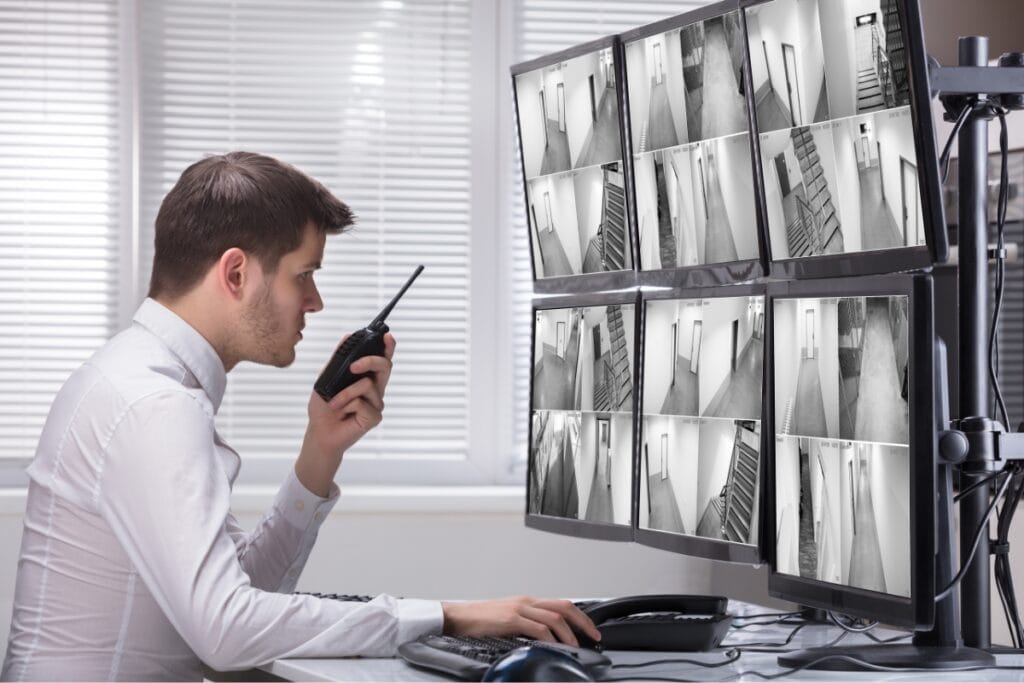 In an office setting, a diligent corporate security officer monitors multiple camera feeds on several screens while communicating efficiently via walkie-talkie.