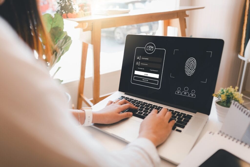 A person types on a laptop displaying a corporate security login screen, complete with a fingerprint icon and input fields for username and password.