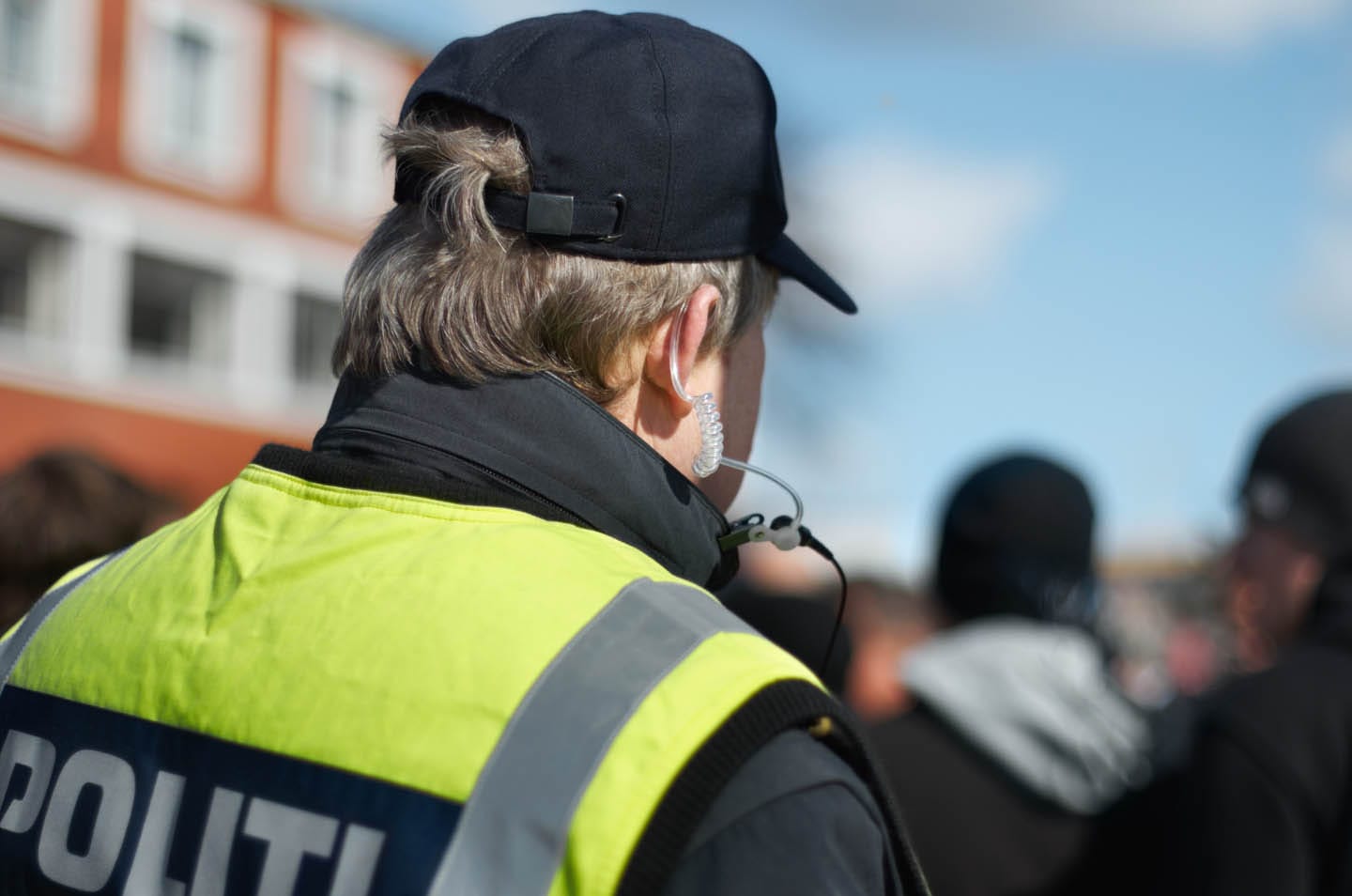 A police officer wearing a cap and high-visibility vest stands in a crowd outdoors, exemplifying the essence of personal safety.