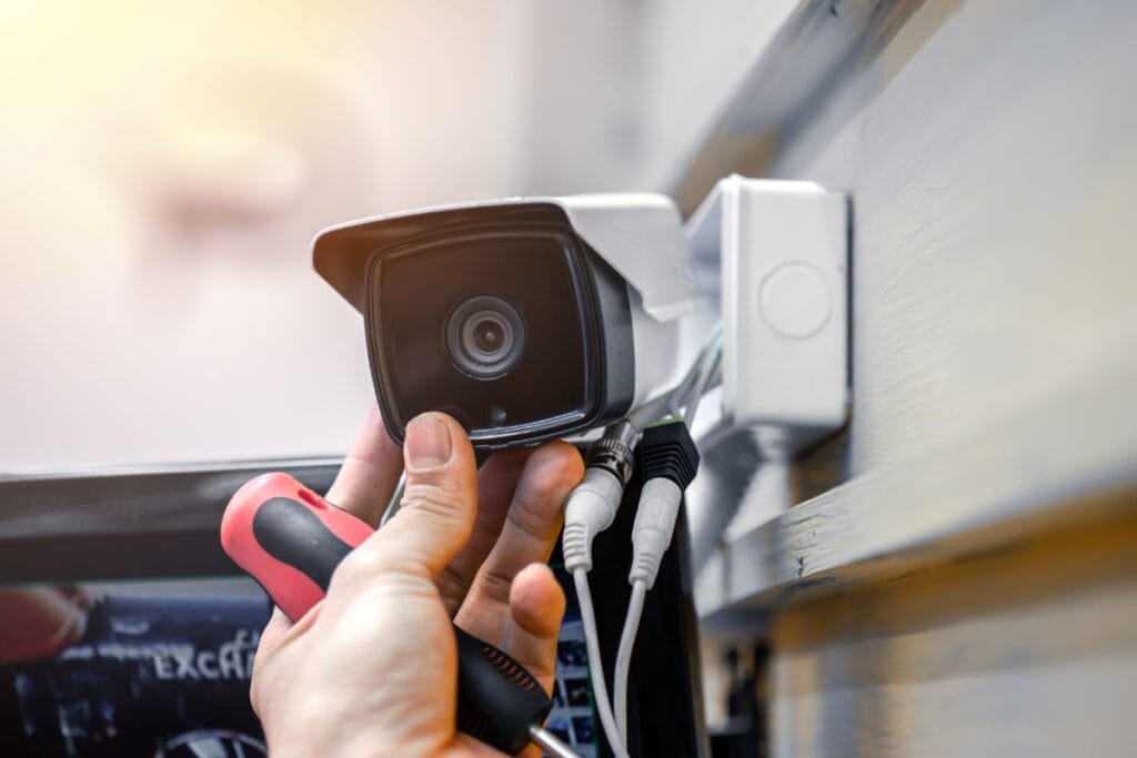 A person carefully adjusts a mounted security camera on the wall, screwdriver in hand, ensuring every angle is covered for comprehensive family law investigations.