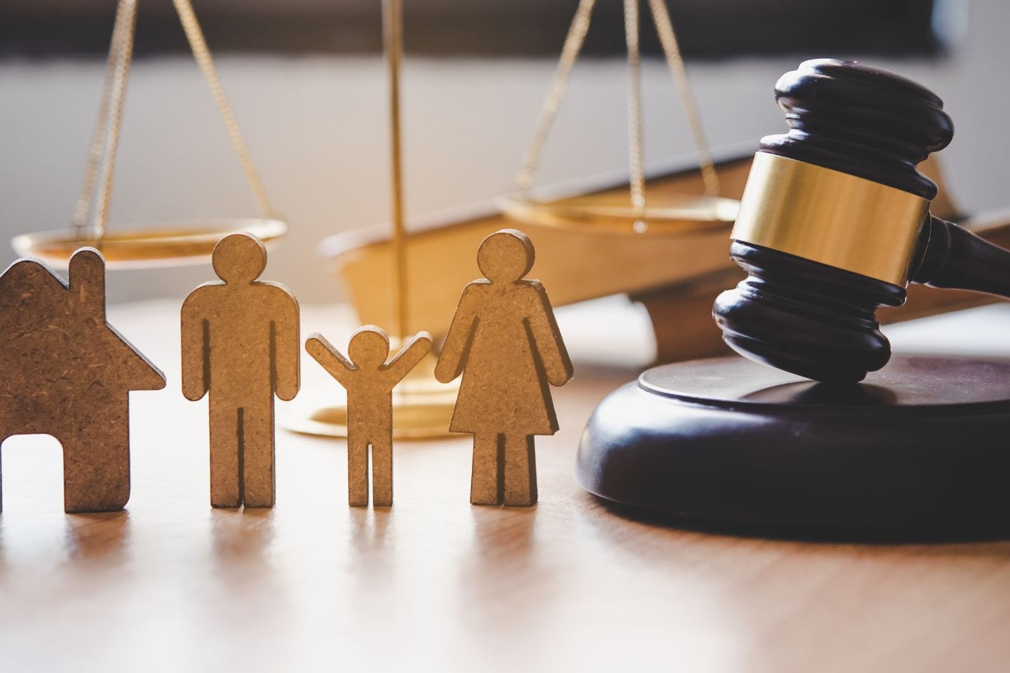 Wooden figures of a family and a house are placed near a gavel and scales of justice, symbolizing legal investigations related to family law and real estate.