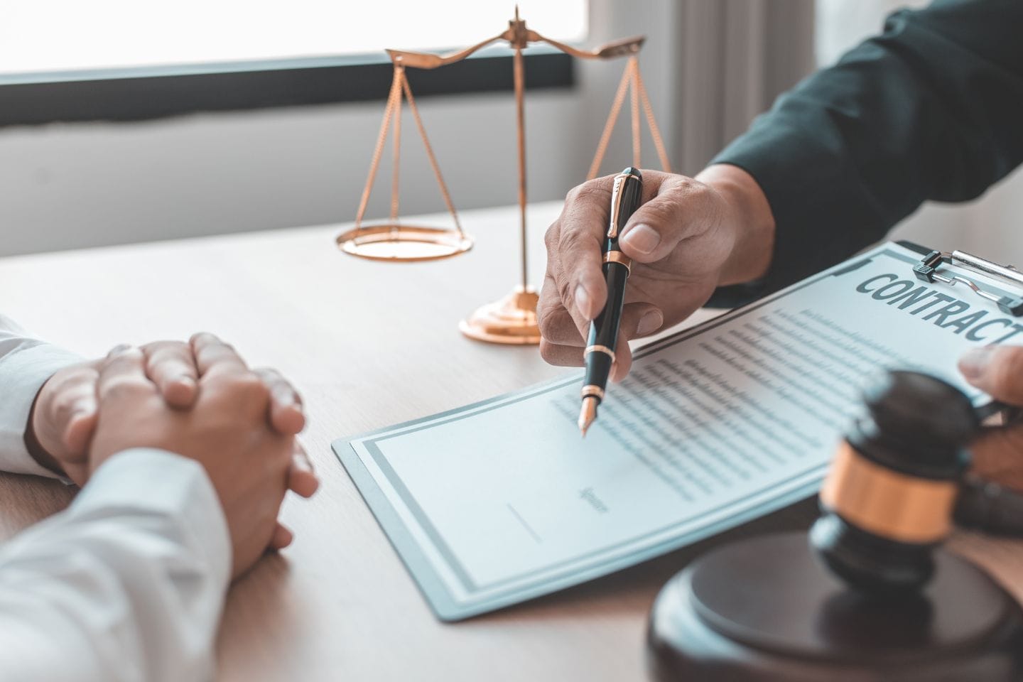 Two people sit at a table discussing a contract, one pointing at the document with a pen. Nearby, a gavel and scales of justice symbolize the weight of family law investigations in this pivotal moment.