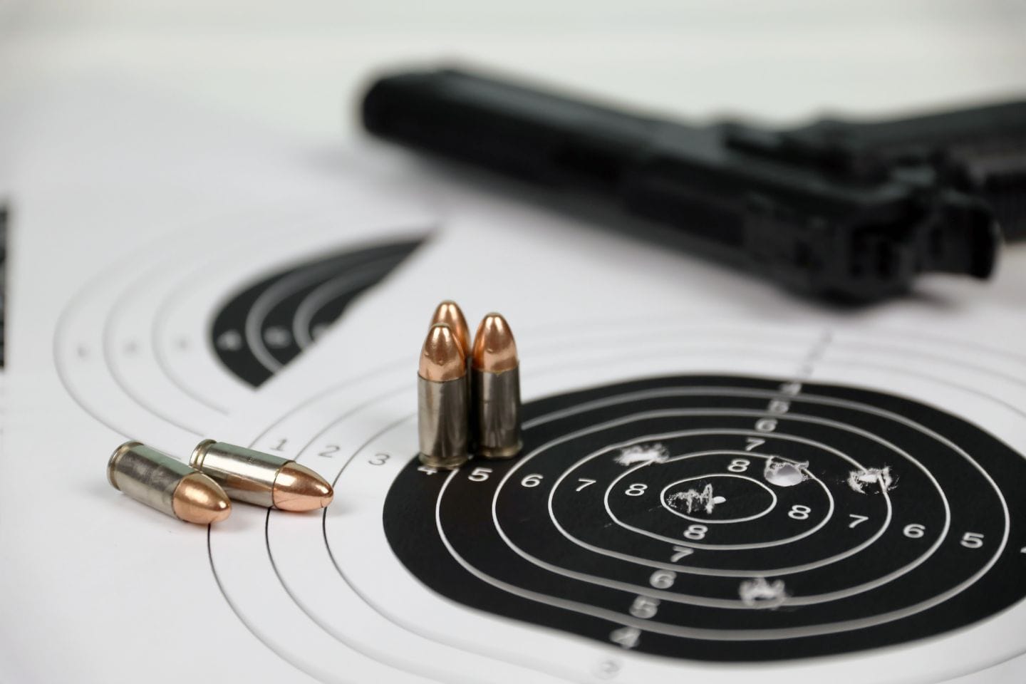 Bullets mark the target sheet, silently narrating the story of active threat training, with a gun positioned in the backdrop amid evidence of practiced precision.