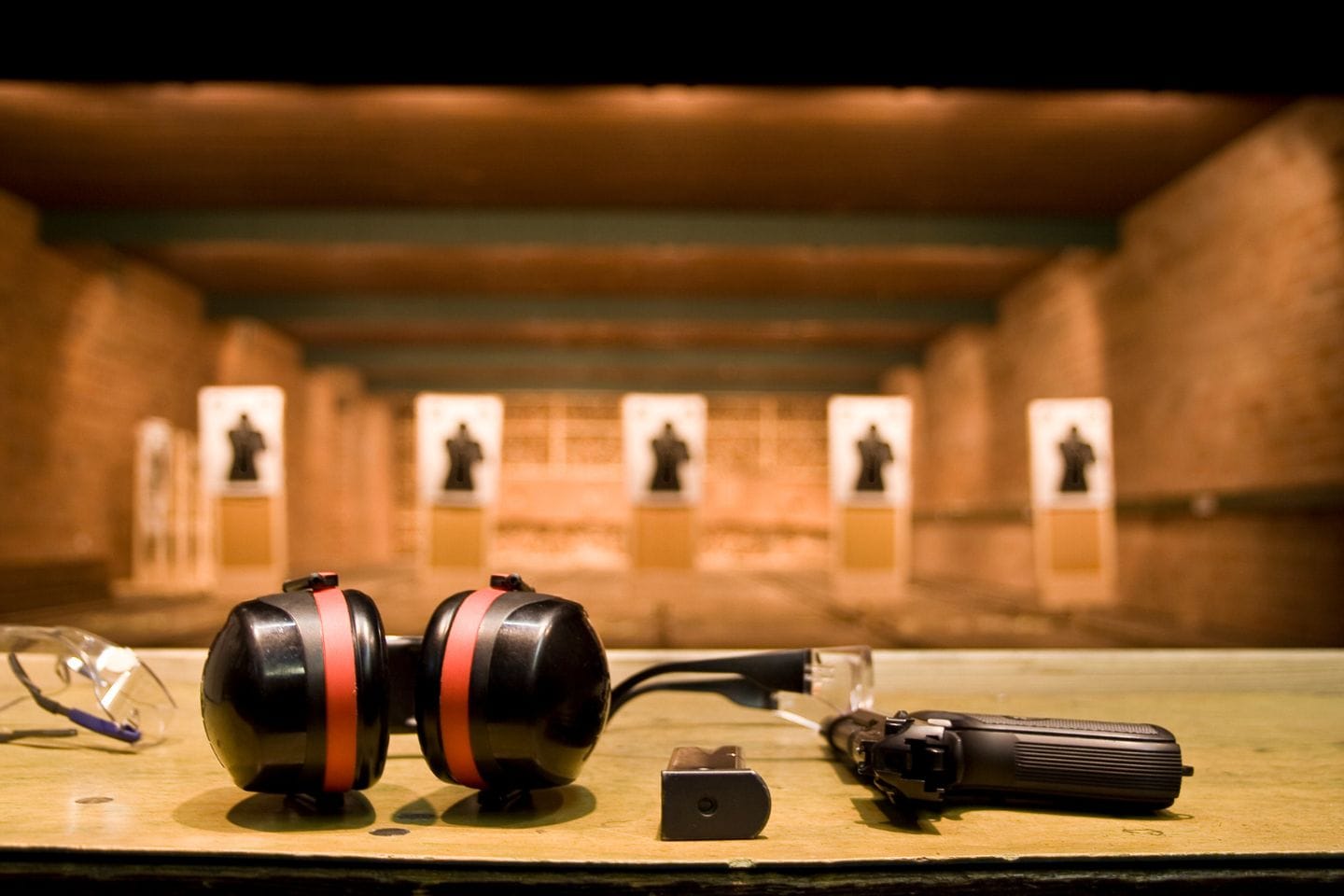 A shooting range with earmuffs, a pistol, and safety glasses on a table in the foreground serves as a perfect setup for active threat training. Targets are visible in the background.