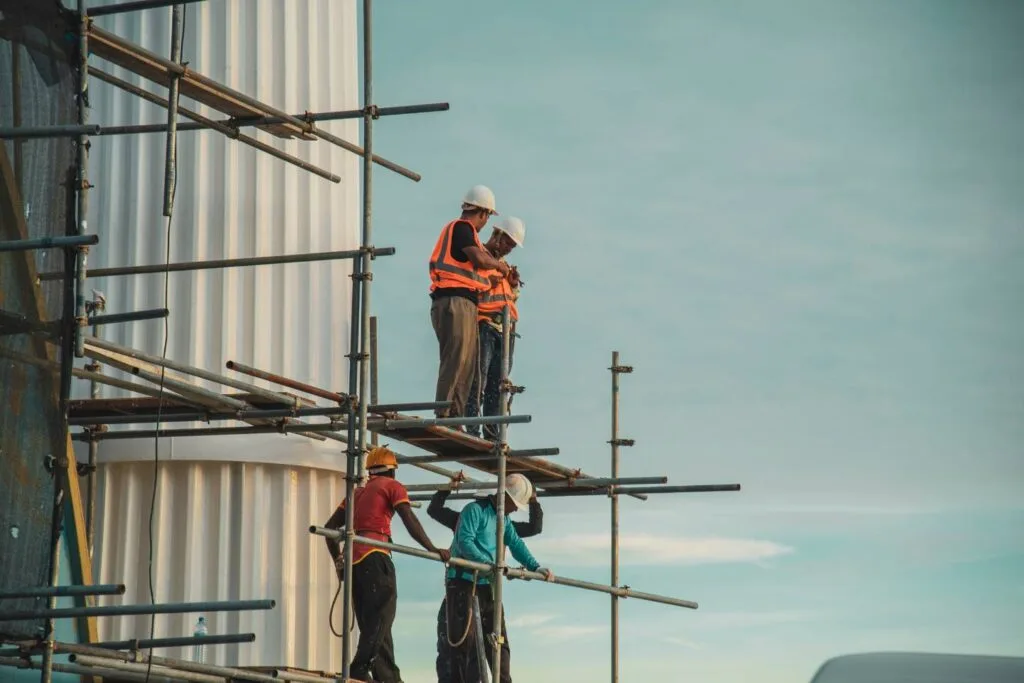 Construction workers wearing safety gear stand on scaffolding against a clear sky, embodying the diverse industries served by their expertise and dedication.