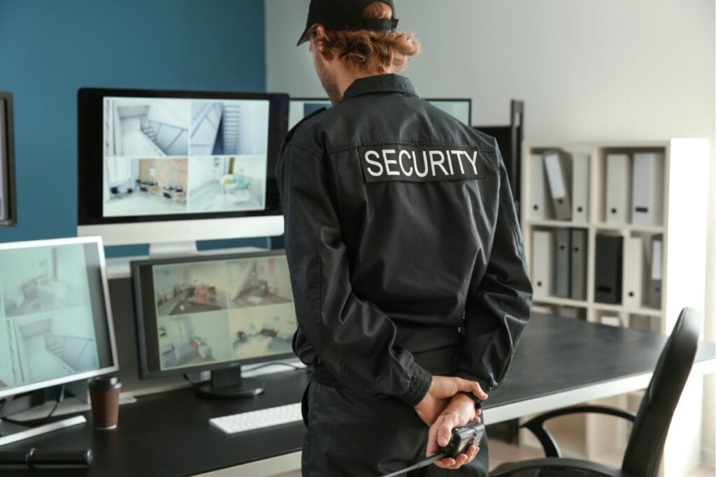 A security guard in professional uniform diligently monitors multiple surveillance screens, embodying a top-tier security service in the office.