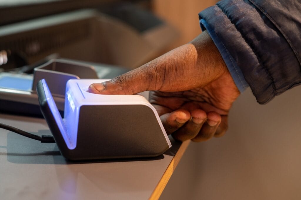 A person presses their thumb on a biometric fingerprint scanner at a counter, highlighting the use of advanced surveillance services.
