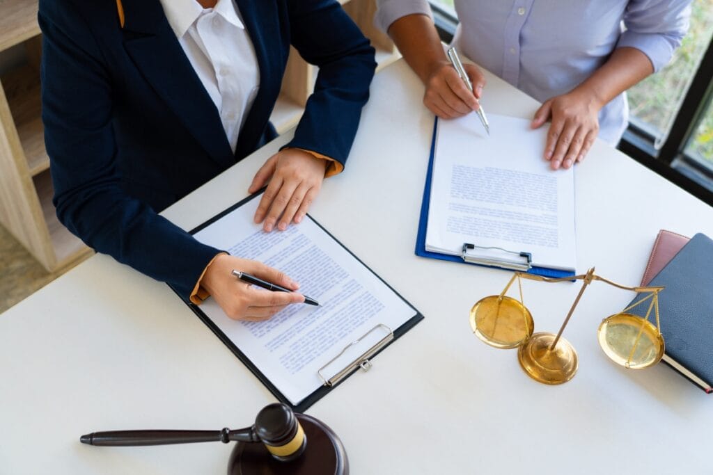 Litigation Support Investigations: How Private Investigators Assist Attorneys 1 Two people sitting at a desk, reviewing and signing legal documents, with a gavel and scales of justice on the table—ideal for illustrating Litigation Support or Investigations in a legal setting.