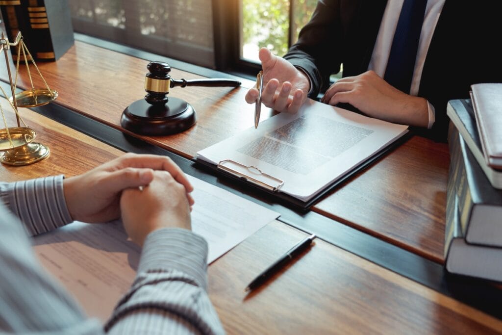 Litigation Support Investigations: How Private Investigators Assist Attorneys 5 Two people in formal attire sit at a desk discussing documents, with a gavel and legal books visible, suggesting a litigation support investigations or business meeting.