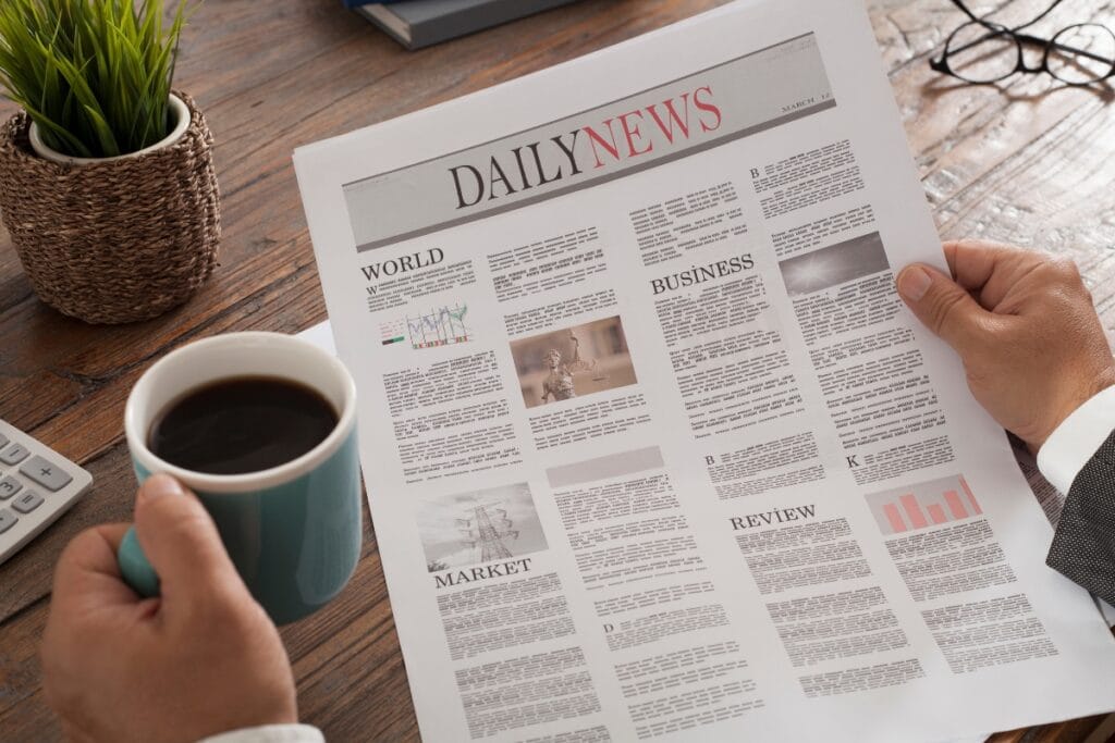 Active Threat Training for Homeowners: How to Stay Prepared for Emergencies 6 Person holding a cup of coffee and reading a newspaper titled “Daily News” at a wooden table with a potted plant, calculator, notebook, and an article on active threat training visible in the background.