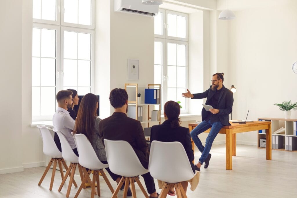 Active Threat Training for Homeowners: How to Stay Prepared for Emergencies 1 A man sits on a desk leading an active threat training discussion with five people seated in chairs, in a bright, modern office setting.