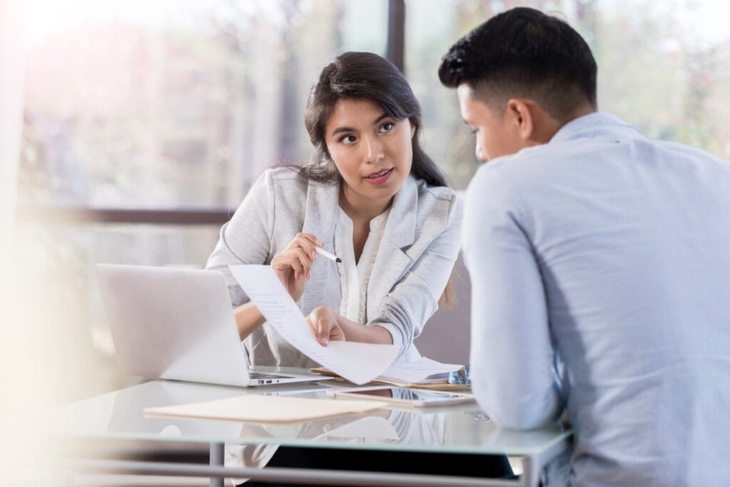 Corporate Investigations: How Businesses Can Detect Fraud and Theft 7 A woman shows a document to a man across a desk while discussing corporate investigations at an office, with a laptop and paperwork in front of them.