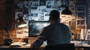 Blog 7 a dimly lit urban office, featuring a focused private investigator scrutinizing evidence on a computer screen, surrounded by photographs and files that suggest a complex infidelity case.