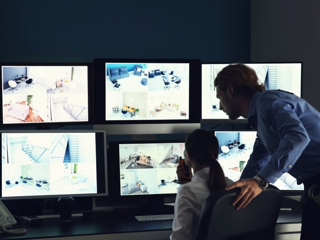 Infidelity Investigations: How Private Investigators Gather Proof of Cheating 8 Two people in a control room monitor multiple security camera feeds on six large screens, carefully analyzing footage for infidelity investigations.