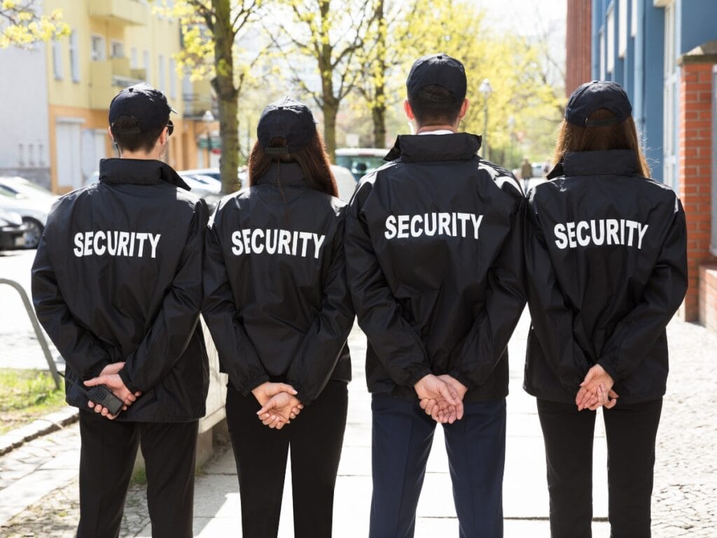 Security Guards in Georgia: Why Demand is Increasing for Business Protection 12 Four security guards in Georgia stand in a row outdoors with their backs to the camera, wearing black jackets and caps labeled "SECURITY.