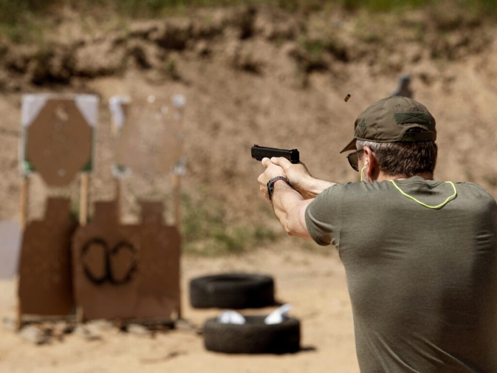 Atlanta Firearm Training: Essential Tips for Responsible Gun Owners 3 A person in a green shirt and cap fires a handgun at cardboard targets outdoors during an Atlanta Firearm Training session, with bullet casings visible in the air.