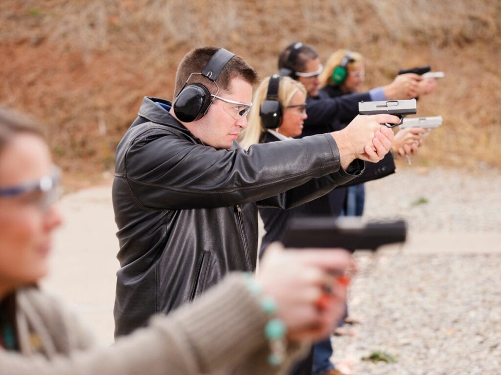 Atlanta Firearm Training: Essential Tips for Responsible Gun Owners 5 A group of people wearing protective gear stand in a line at an outdoor shooting range, participating in Atlanta Firearm Training as they aim handguns at targets.