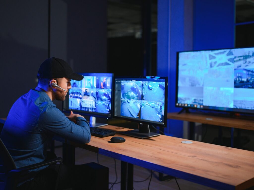 Business Fraud Investigations: How Private Investigators Help Protect Your Company 5 A person wearing a headset monitors multiple security camera feeds on computer screens in a dimly lit control room, assisting with business fraud investigations.