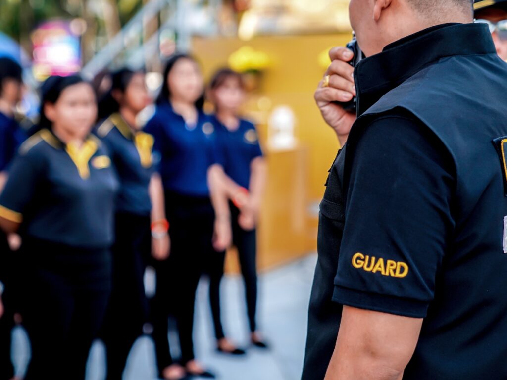 Holiday Event Security: How Security Guards Keep Large Gatherings Safe 3 A security guard with a radio stands in the foreground, ensuring Holiday Event Security, while a group of people in uniforms are lined up in the background.