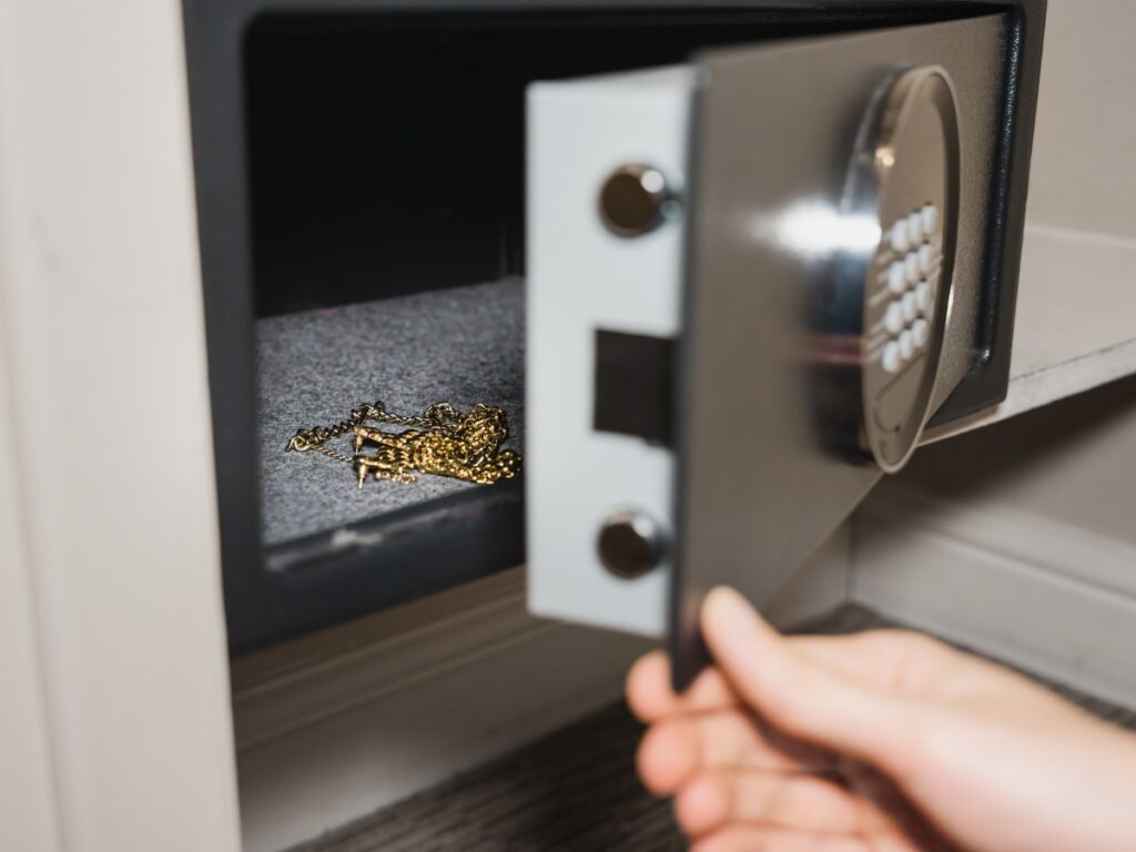 A person opens a small safe containing gold jewelry or chains inside, showcasing the importance of including safes in your home security checklist.