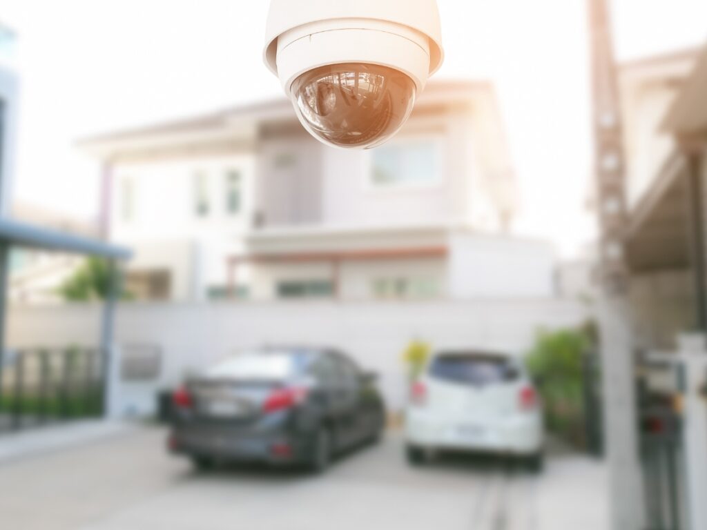 A security camera mounted above a driveway monitors two parked cars in front of a residential building during daylight, fulfilling one important item on any home security checklist.